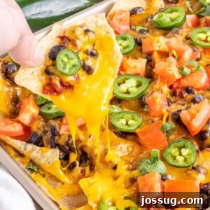 Hand lifting a loaded nacho from a sheet pan, showing the rich toppings and melted cheese.