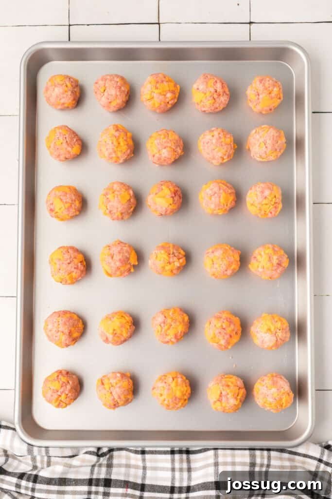Cheesy Sausage Balls 8 Walnut-sized sausage balls neatly arranged in rows on a baking sheet, ready for the oven.