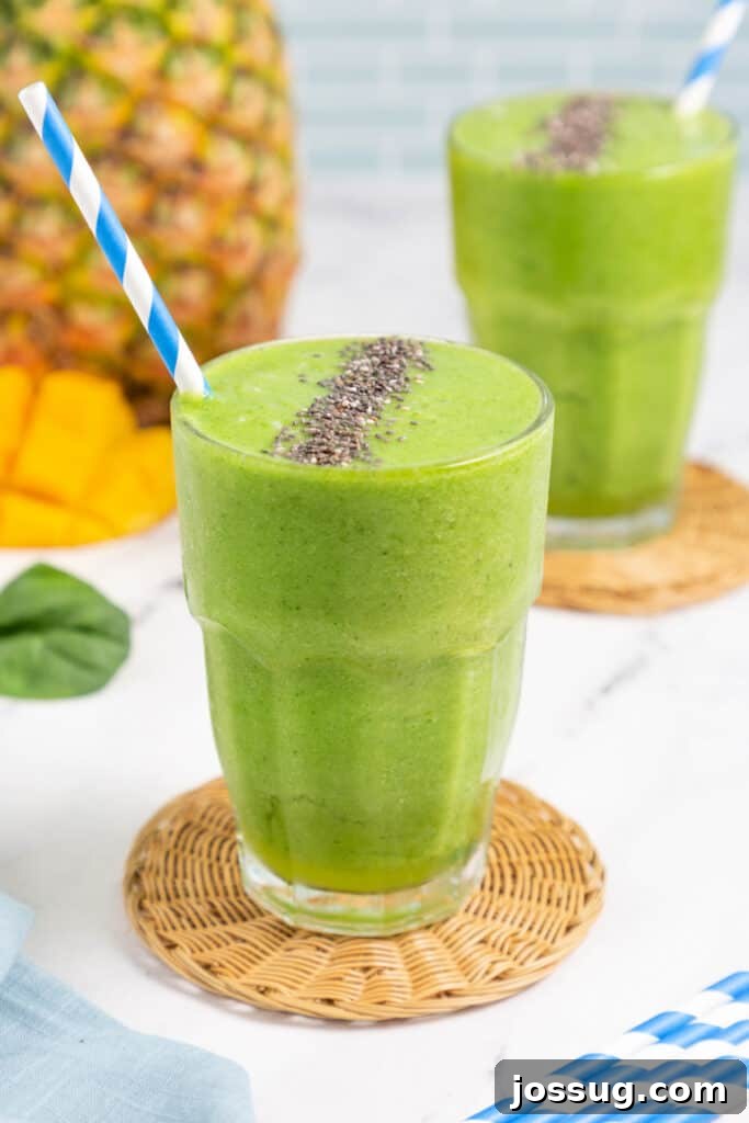 glass filled with pineapple green smoothie, garnished with a pineapple slice and a straw