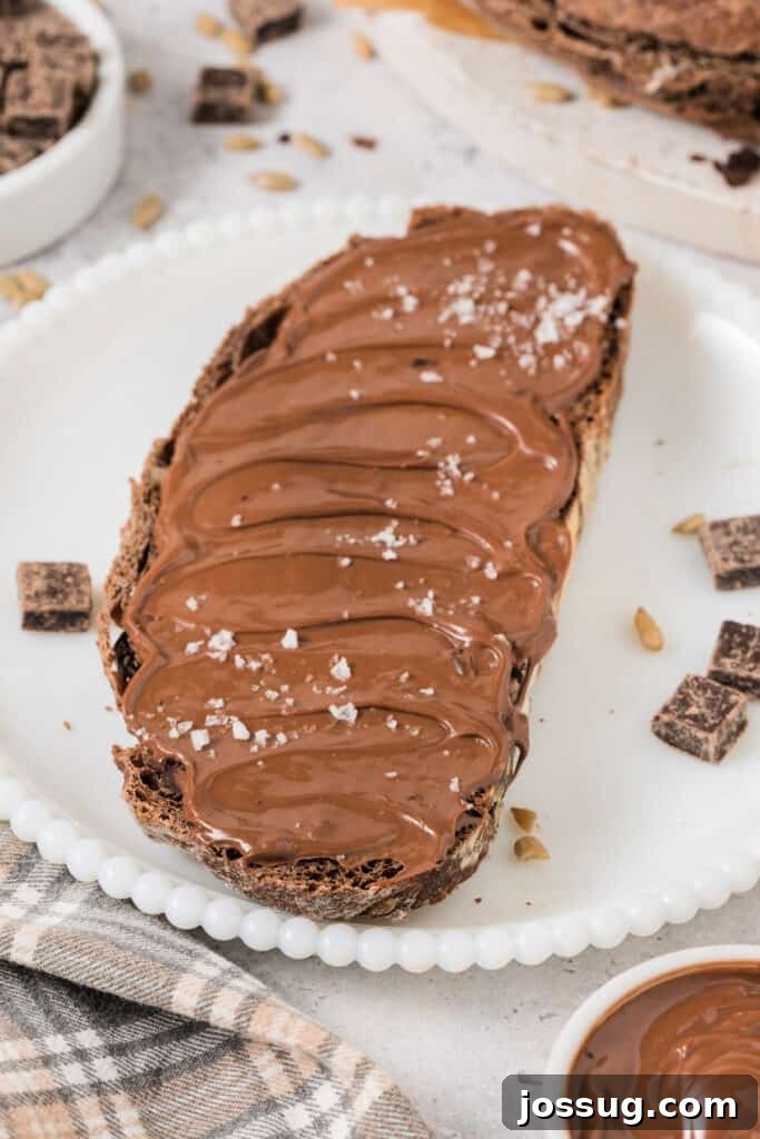 A slice of chocolate no-knead bread generously spread with Nutella and sprinkled with sea salt, on a white plate