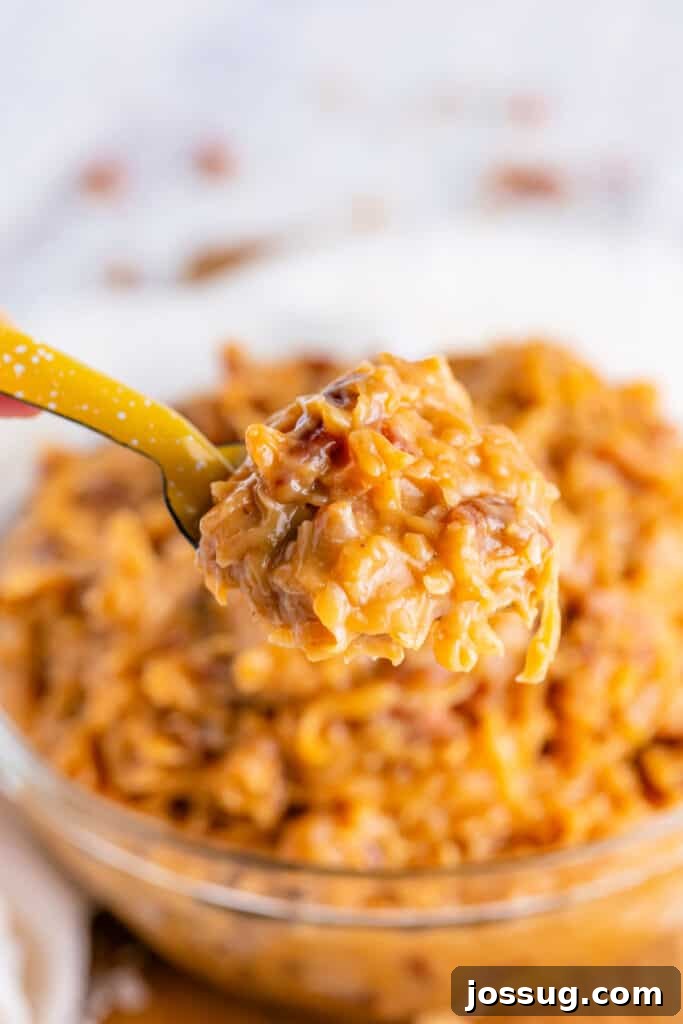 Toasted Coconut Pecan Frosting 4 A close-up shot of a spoon filled with rich, golden-brown Coconut Pecan Frosting, showing its thick and inviting texture with clearly visible coconut flakes and chopped pecans.