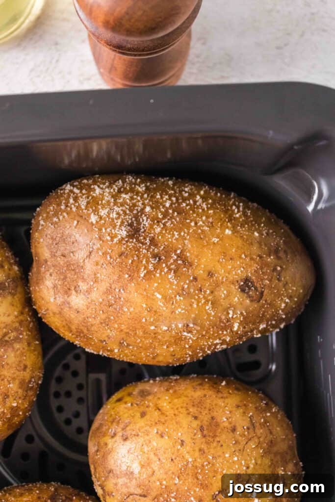 Crispy Air Fryer Spuds 4 Oiled and seasoned Russet potatoes placed neatly in an air fryer basket, ready for cooking.