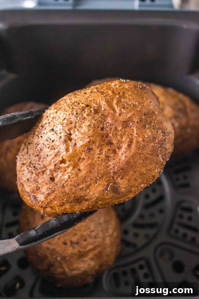 Crispy Air Fryer Spuds 5 Tongs carefully holding an air fryer baked potato over the air fryer basket after cooking.