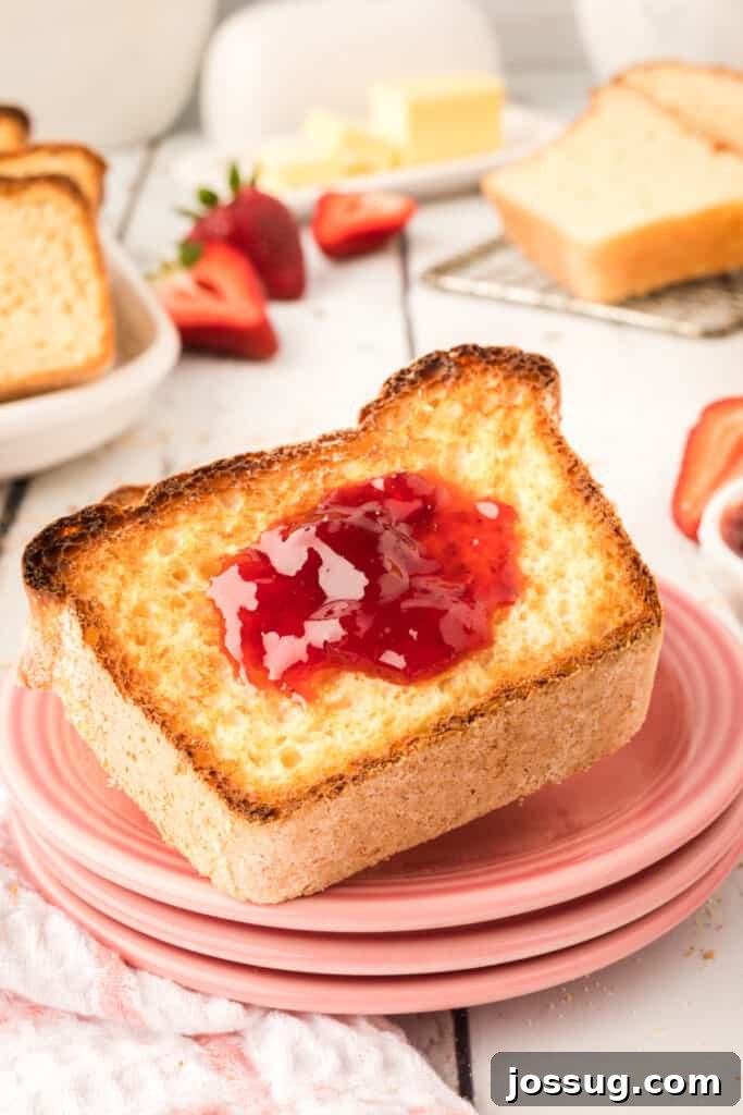 A perfectly toasted slice of homemade English Muffin Bread, generously spread with bright red jam, ready to be enjoyed.