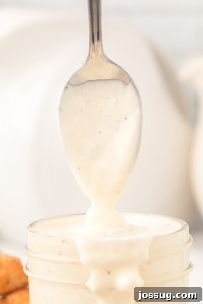 Creamy Dill & Caper Dressing 4 Close-up of creamy tartar sauce dripping off a spoon into a glass jar, highlighting its texture.