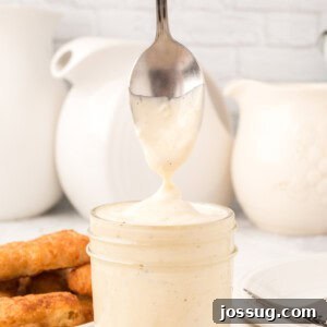 Close-up of homemade tartar sauce in a jar with some scooped onto a spoon, showing its creamy texture.