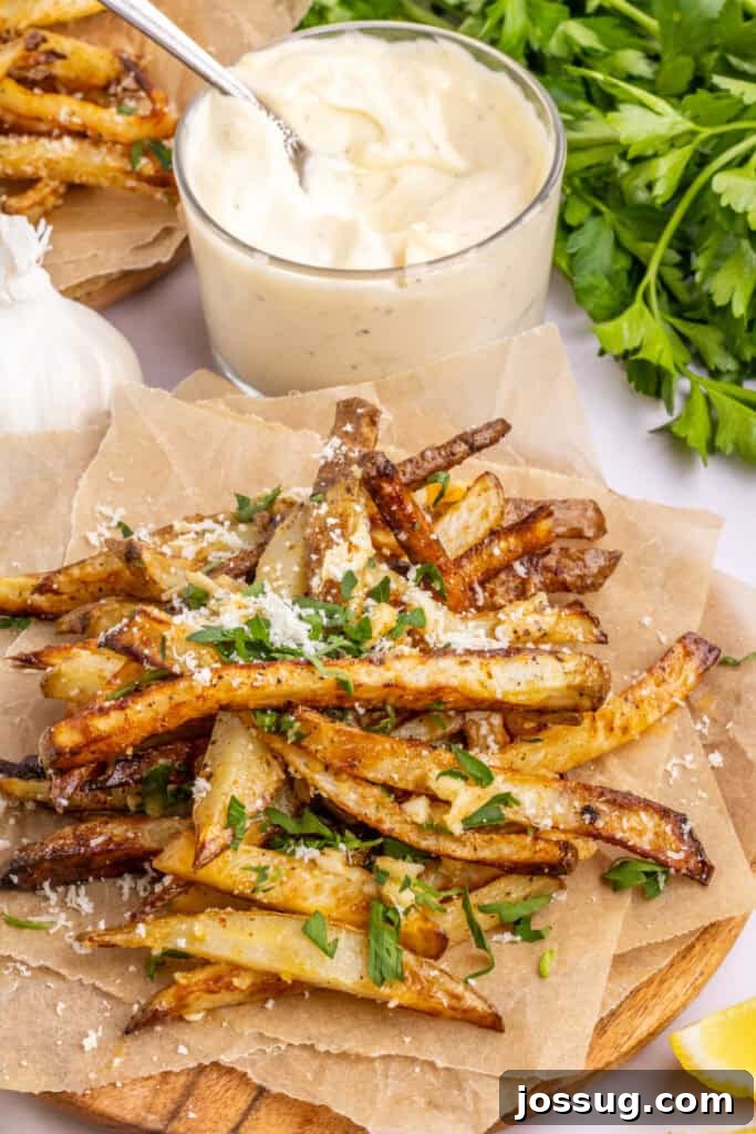 A delectable pile of crispy Air Fryer Garlic Parmesan Fries served on parchment paper, with a bowl of creamy garlic aioli in the background, ready for dipping.