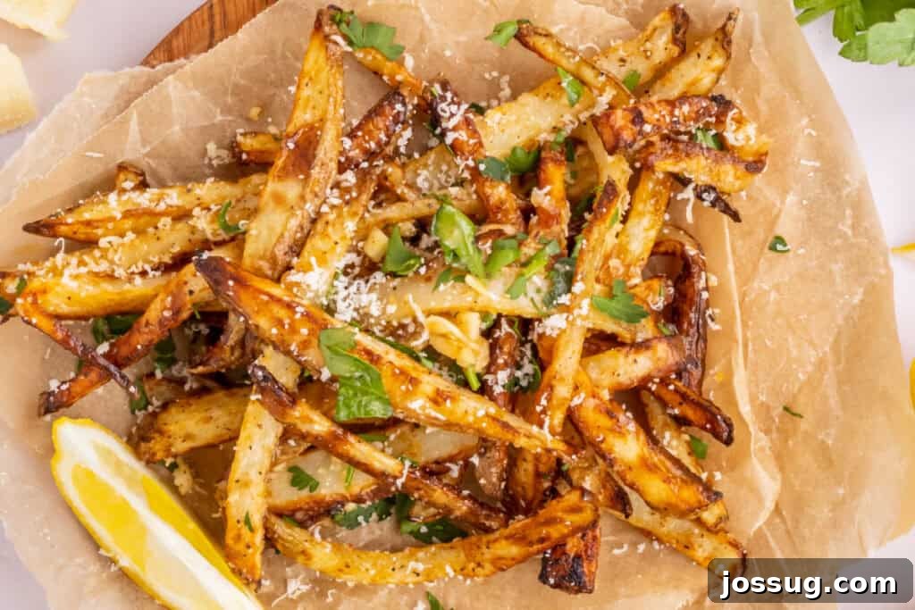 A top-down view of cooked garlic parmesan fries scattered appealingly on brown parchment paper, highlighting their golden hue and texture.