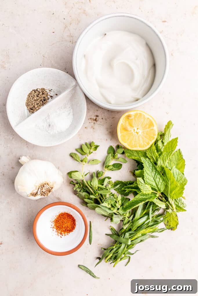Mediterranean Potato Wedge Feast 4 Ingredients for creamy herb sauce, including plain Greek yogurt, fresh mint, oregano, tarragon, garlic cloves, lemon wedges, and a sprinkle of sea salt and pepper, arranged around a food processor bowl.