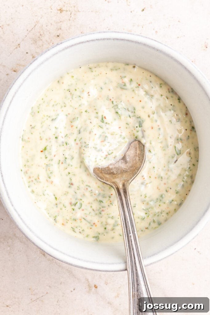 Mediterranean Potato Wedge Feast 6 Finished creamy herb yogurt sauce in a small ceramic bowl with a spoon, showing its smooth, rich texture and flecks of green herbs, ready for drizzling.