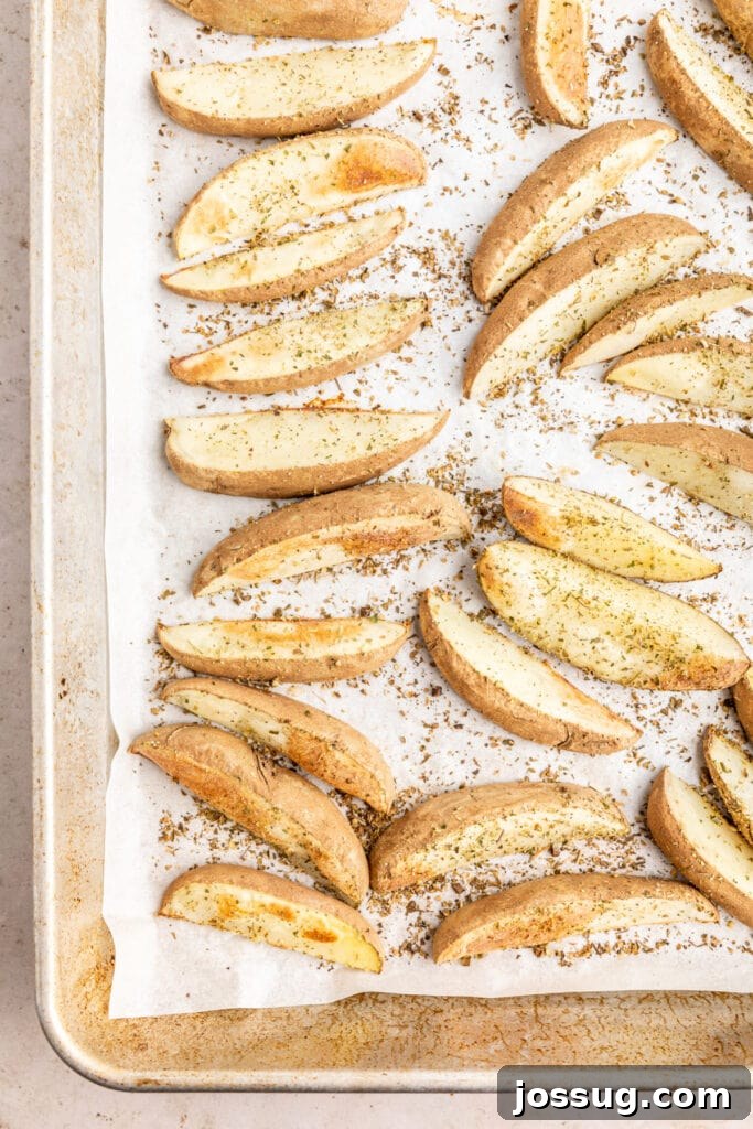 Mediterranean Potato Wedge Feast 7 Seasoned potato wedges arranged in a single layer on a baking sheet lined with parchment paper, perfectly spaced for optimal roasting and crisping, prior to baking.
