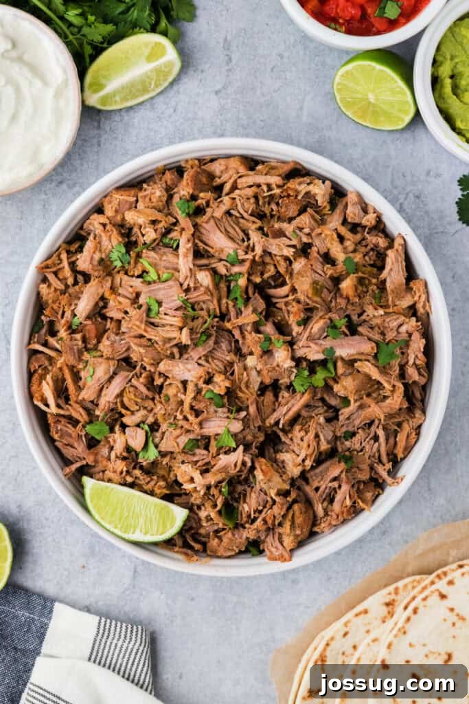 Looking down into a bowl filled with instant pot carnitas, garnished with cilantro and lime wedges.
