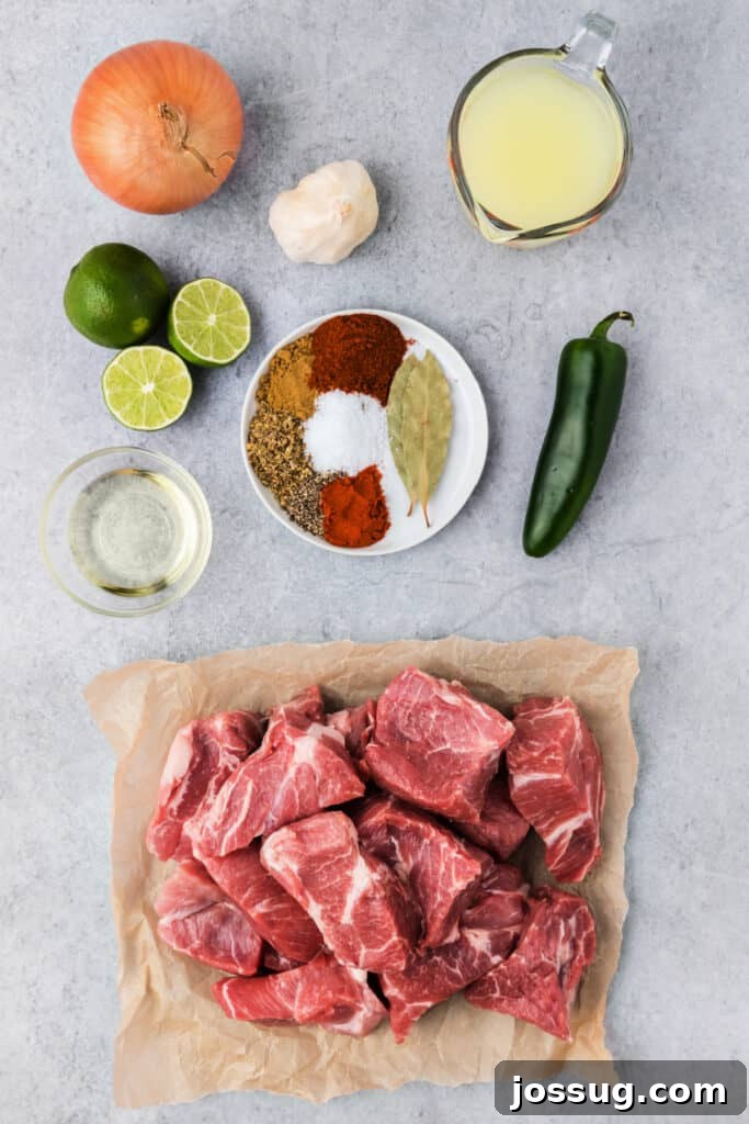 A collection of ingredients laid out to make carnitas, including pork shoulder, onions, jalapeños, garlic, and various spices.
