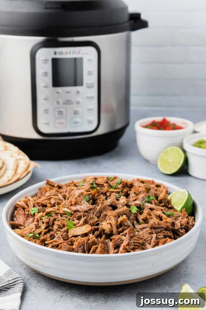 A bowl of freshly cooked carnitas meat sits in front of an Instant Pot, with steam gently rising.