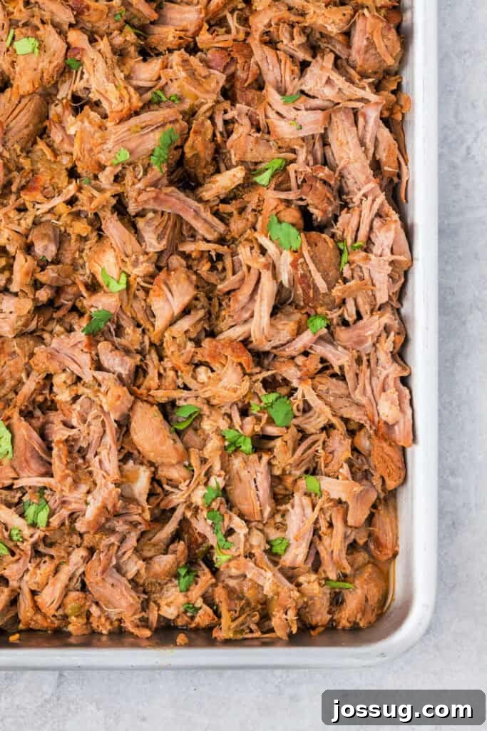 A closeup of a sheet pan filled with cooked Mexican carnitas meat, showing the tender shredded pork with crispy browned edges.