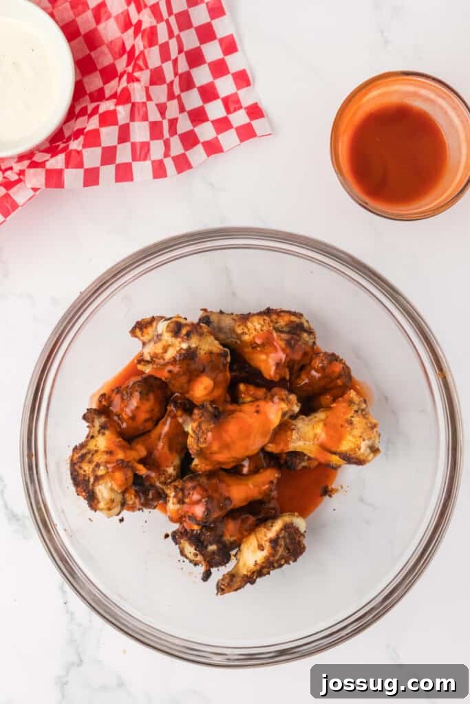 Perfectly Crispy Air Fryer Buffalo Wings 8 Buffalo sauce being poured over cooked seasoned chicken wings in a bowl
