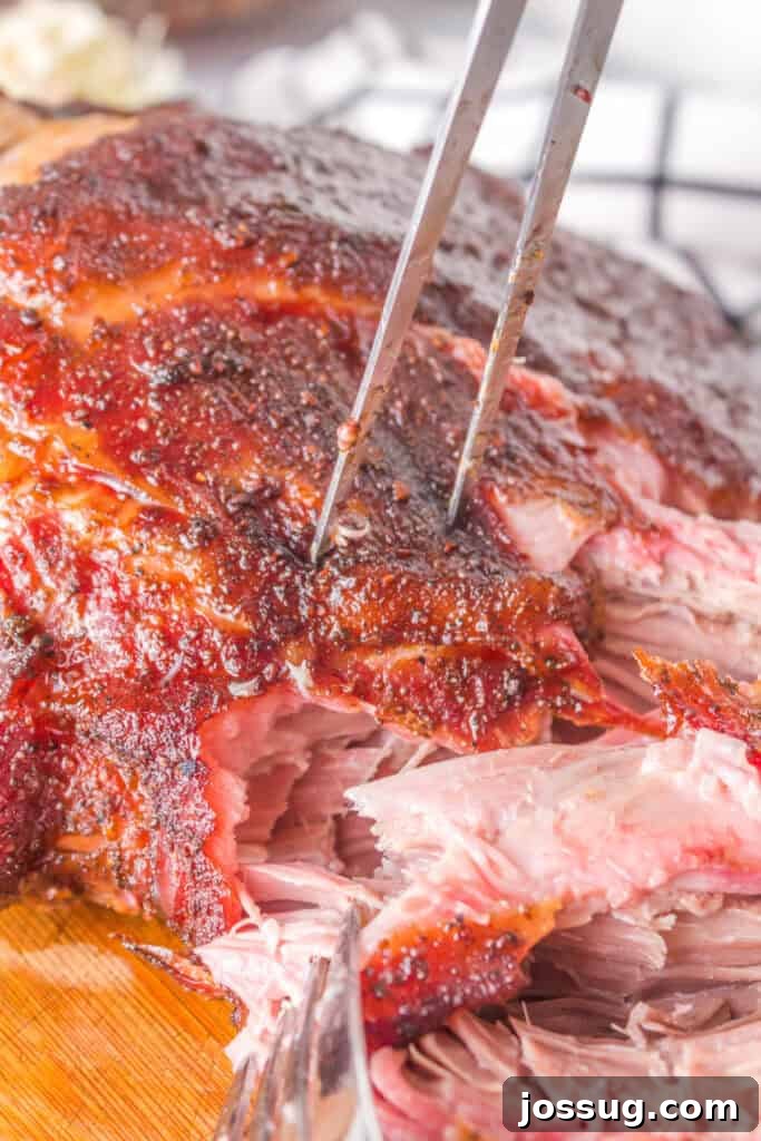 Forks shredding into tender, juicy grilled pulled pork on a cutting board, demonstrating the perfect texture.