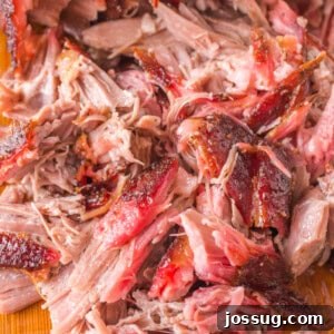 Square crop of juicy shredded pulled pork with visible bark and smoke ring, ideal for a recipe card.