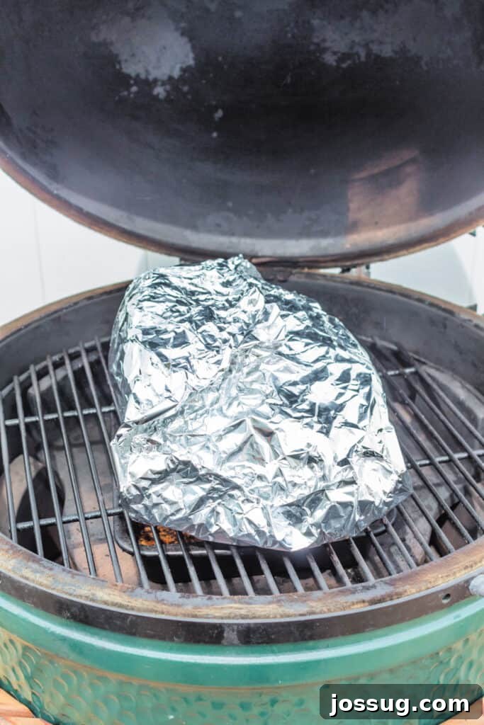 Boston butt tightly wrapped in foil on the grill to finish cooking, illustrating the 'Texas Crutch' method.