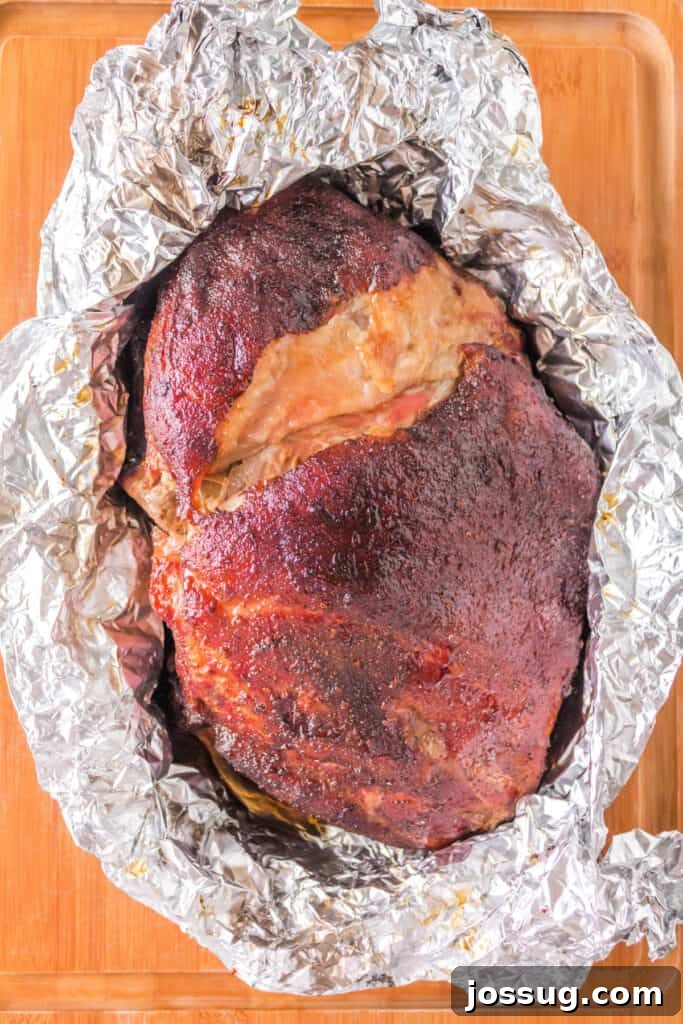 Finished Boston butt resting in foil on a wooden cutting board, allowing juices to redistribute.