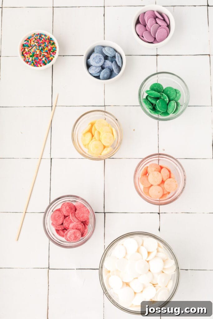 A flat lay photograph displaying all the colorful ingredients needed to make rainbow candy bark, including white chocolate, various shades of candy melts, and a bowl of sprinkles.