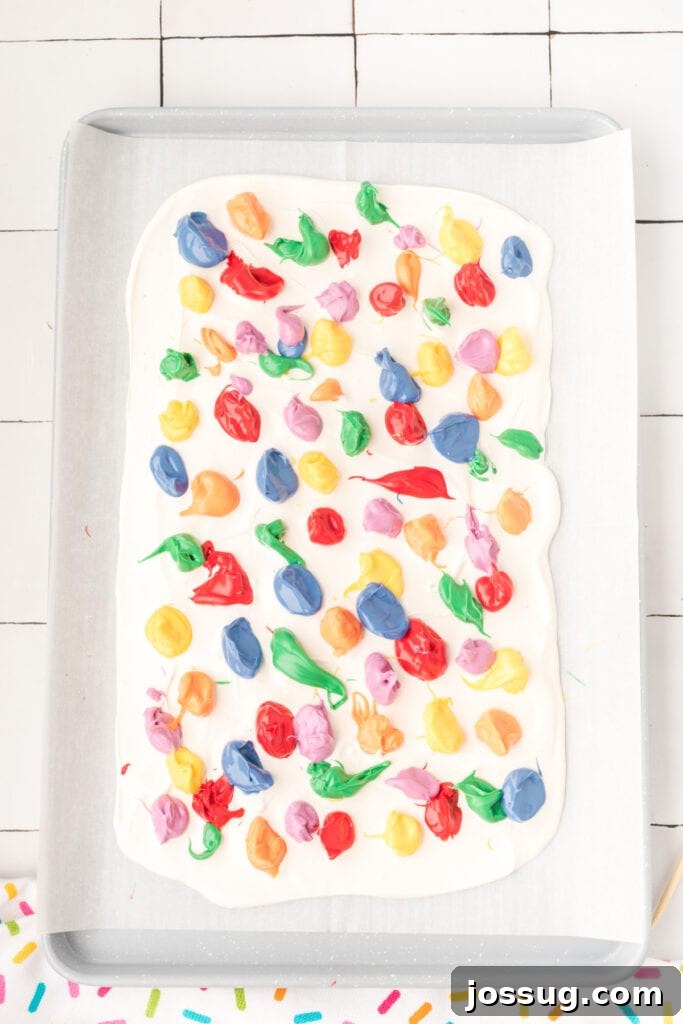 Vibrant red candy melts being drizzled in lines over the smooth white chocolate base, preparing for the full rainbow layering of the candy bark.