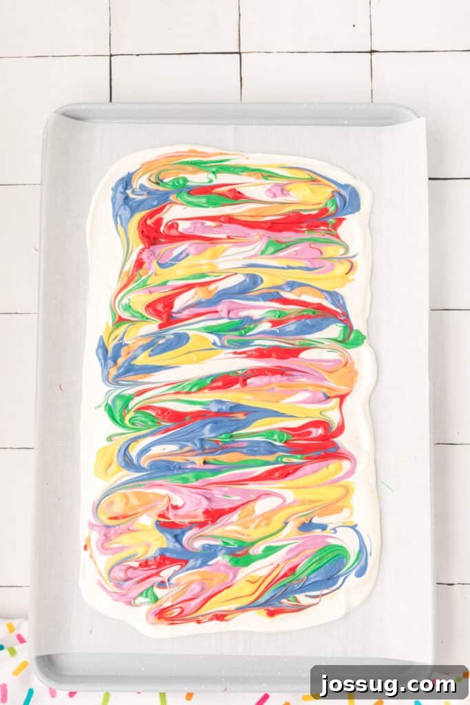 A toothpick gently swirling vibrant candy melts into the white chocolate base, creating beautiful, distinct patterns for the rainbow candy bark.