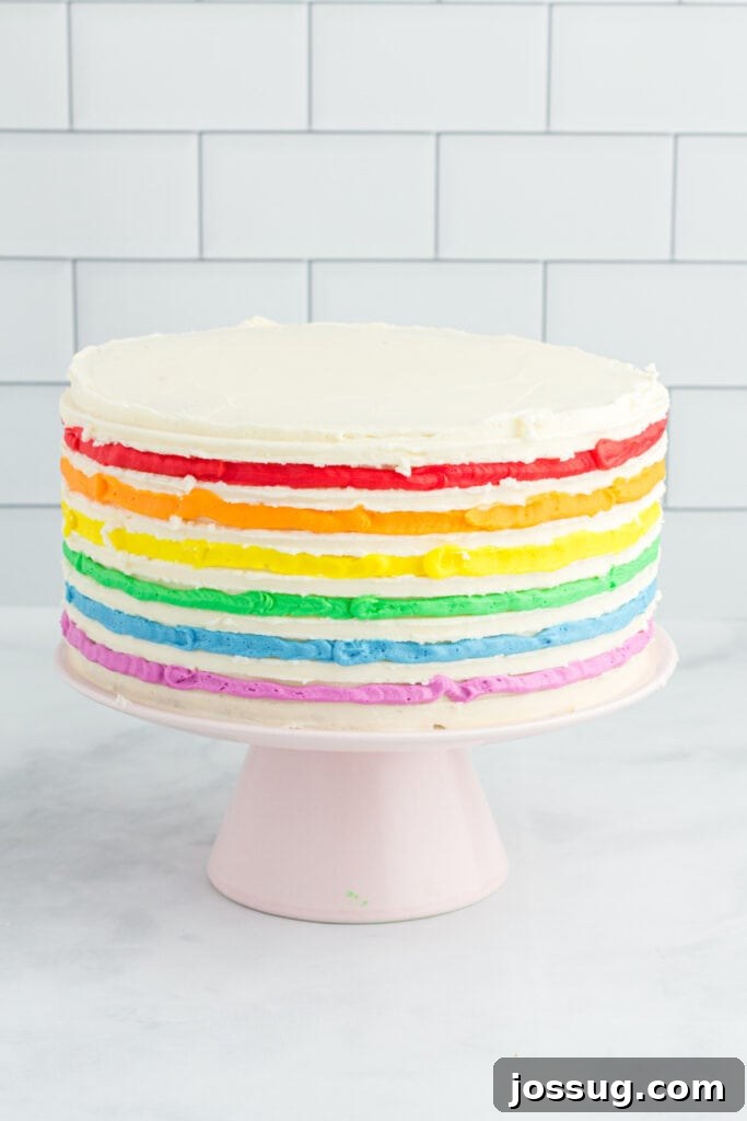 A fully decorated Rainbow Striped Funfetti Cake with elegant frosting swirls on top, presented on a cake stand.