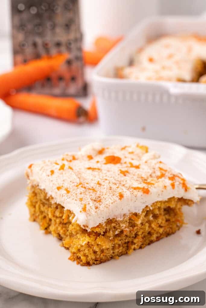 A perfectly sliced piece of moist carrot cake topped with creamy cream cheese frosting, served on a white plate