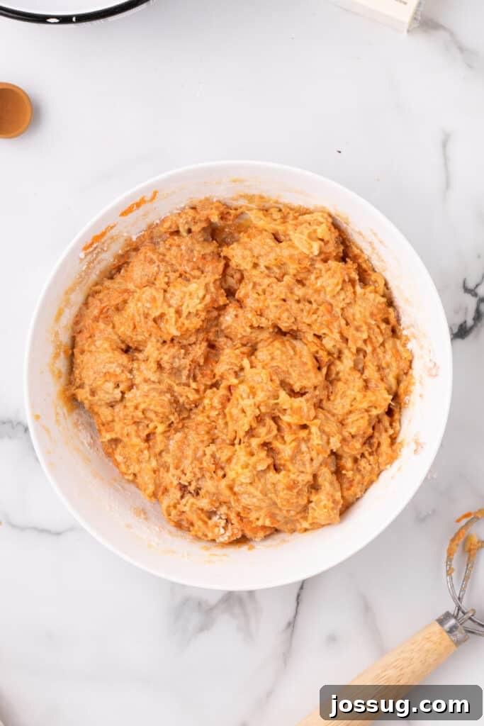 Cake batter mixed thoroughly in a large mixing bowl, showcasing the flecks of grated carrot and pineapple within the smooth consistency