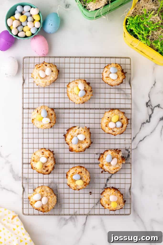 Freshly baked coconut Easter nests, perfectly golden brown, are cooling on a wire rack after being shaped. Some are already filled with colorful candy eggs, showcasing the finished treat.