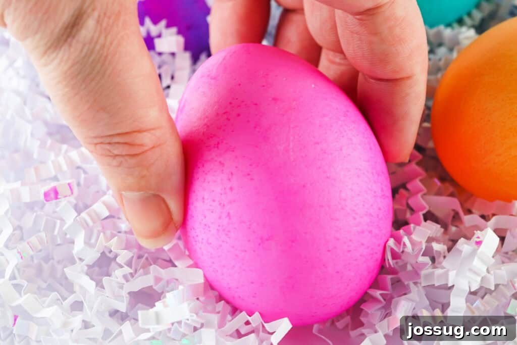 Hand holding a vibrant pink food coloring dyed Easter egg