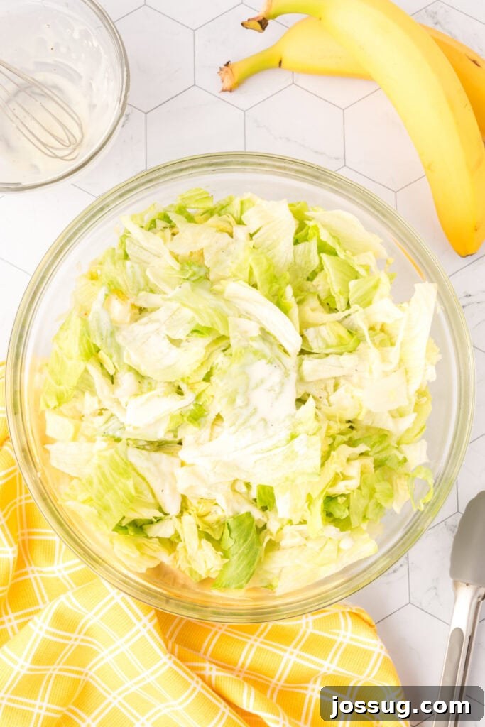 Grandma's Banana Lettuce Salad 5 Dressing being mixed into crisp iceberg lettuce in a bowl.