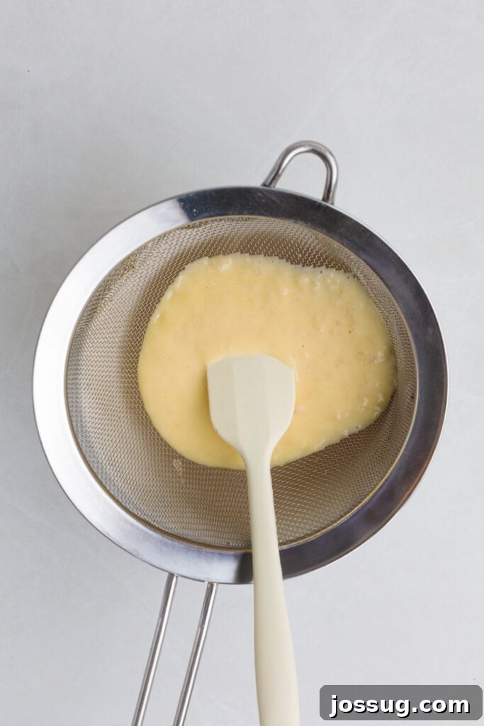 Zesty Lemon Butter Drizzle 6 Straining the finished lemon butter sauce through a fine wire mesh strainer to remove shallots and achieve an ultra-smooth consistency.