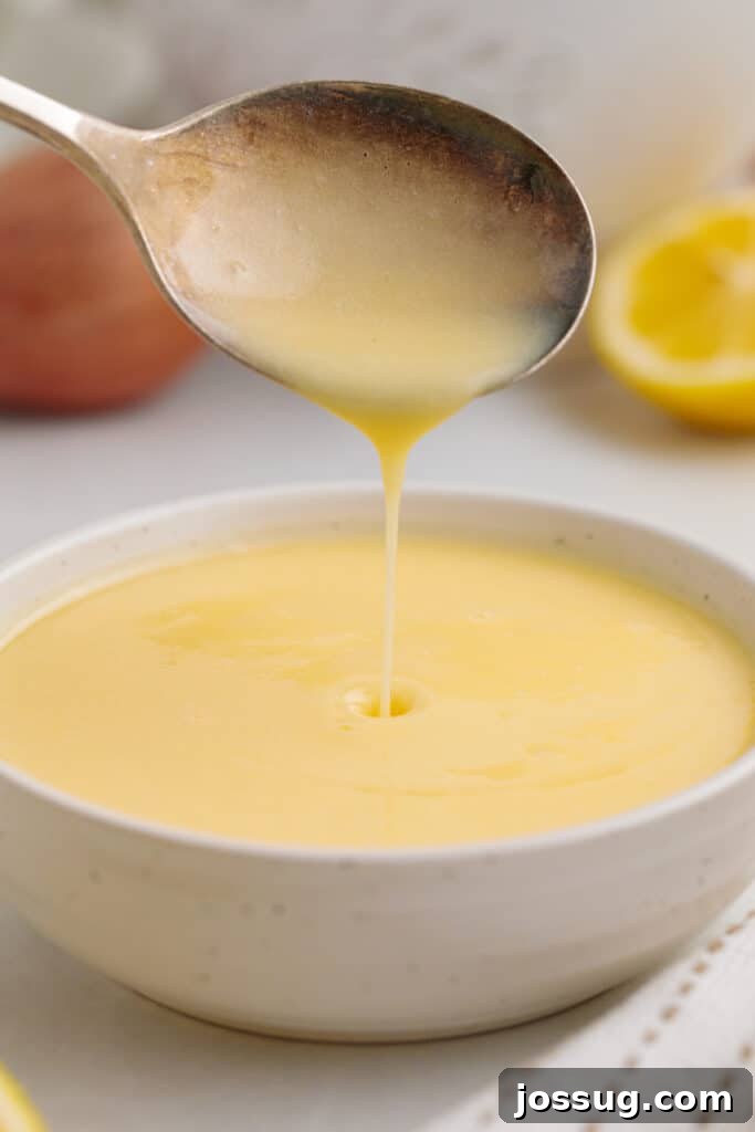 Zesty Lemon Butter Drizzle 8 Closeup of creamy lemon butter sauce being elegantly poured from a spoon into a small serving bowl, showcasing its smooth texture.