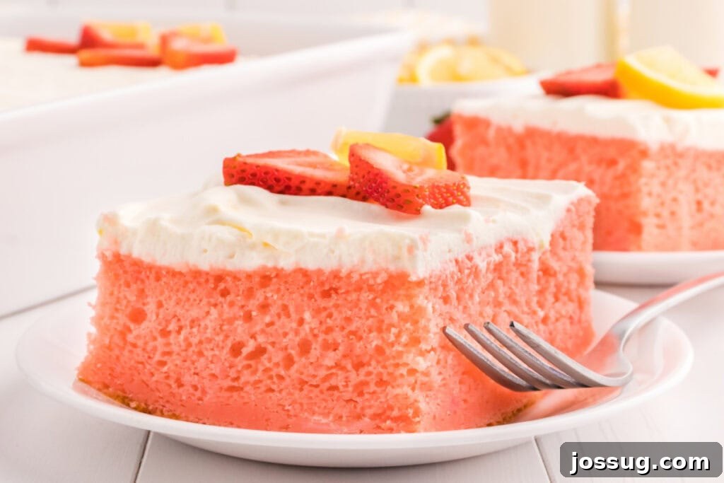 A perfect slice of strawberry cake with a generous dollop of lemon cream topping, garnished with a fresh strawberry and lemon slice, elegantly presented on a white plate.