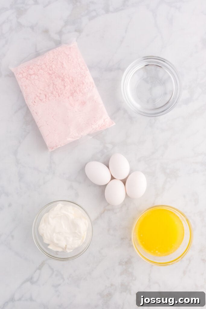 Assorted baking ingredients laid out on a white surface, including a box of strawberry cake mix, sour cream, water, butter, and eggs, ready to be combined for the cake.
