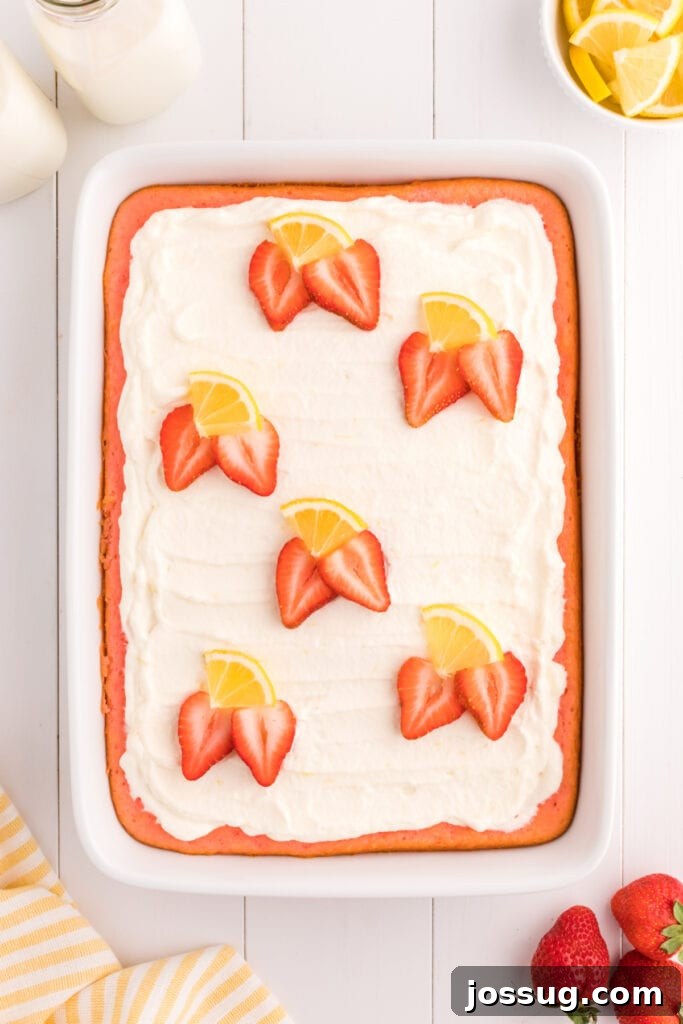 The fully assembled strawberry cake topped with lemon cream, garnished with fresh strawberry halves and lemon slices, ready for serving.