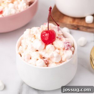 Square-format image of a white bowl filled with fluffy fruit salad, garnished with a maraschino cherry, perfect for social media sharing.