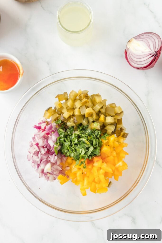Ingredients for Pickle de Gallo in a glass mixing bowl, including chopped pickles, red onion, yellow bell pepper, and fresh cilantro.