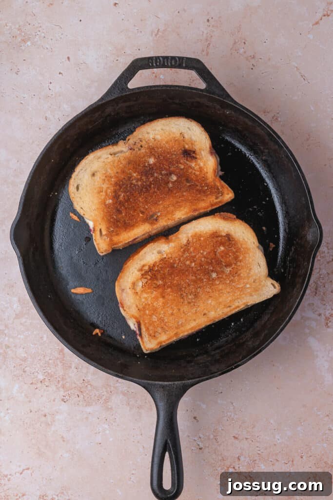 Sweet and Savory Blackberry Grilled Cheese 13 Two golden-brown grilled cheese sandwiches actively cooking in a cast iron skillet, cheese visibly melting