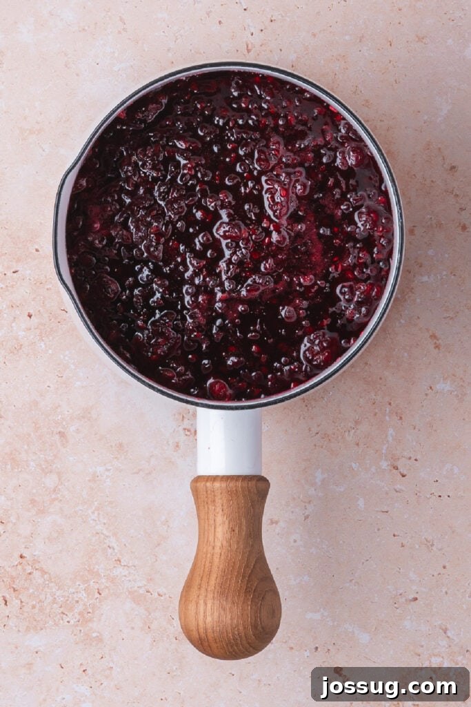 Sweet and Savory Blackberry Grilled Cheese 5 Simmered blackberry jam in a white saucepan with a wooden handle, looking thick and glossy after cooking