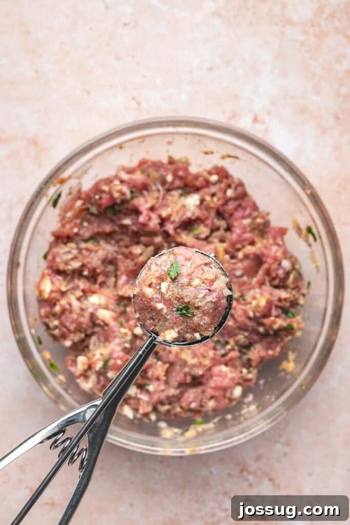 Cookie scoop holding a portion of turkey feta meatball mixture over the bowl