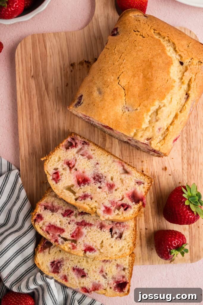 Sweet Strawberry Loaf 2 Two generous slices of moist strawberry bread on a wooden cutting board, garnished with whole fresh strawberries and a sprig of mint, highlighting its juicy berry pieces and golden crust.