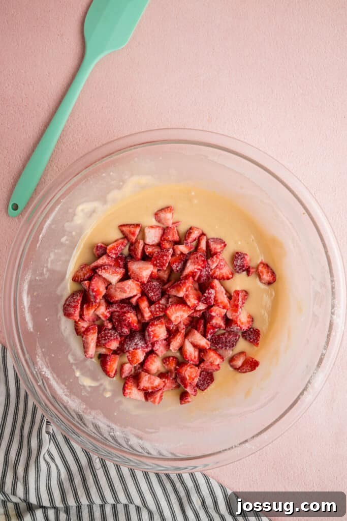Sweet Strawberry Loaf 12 The floured chopped strawberries are gently placed on top of the prepared batter in the glass mixing bowl, poised for careful folding.