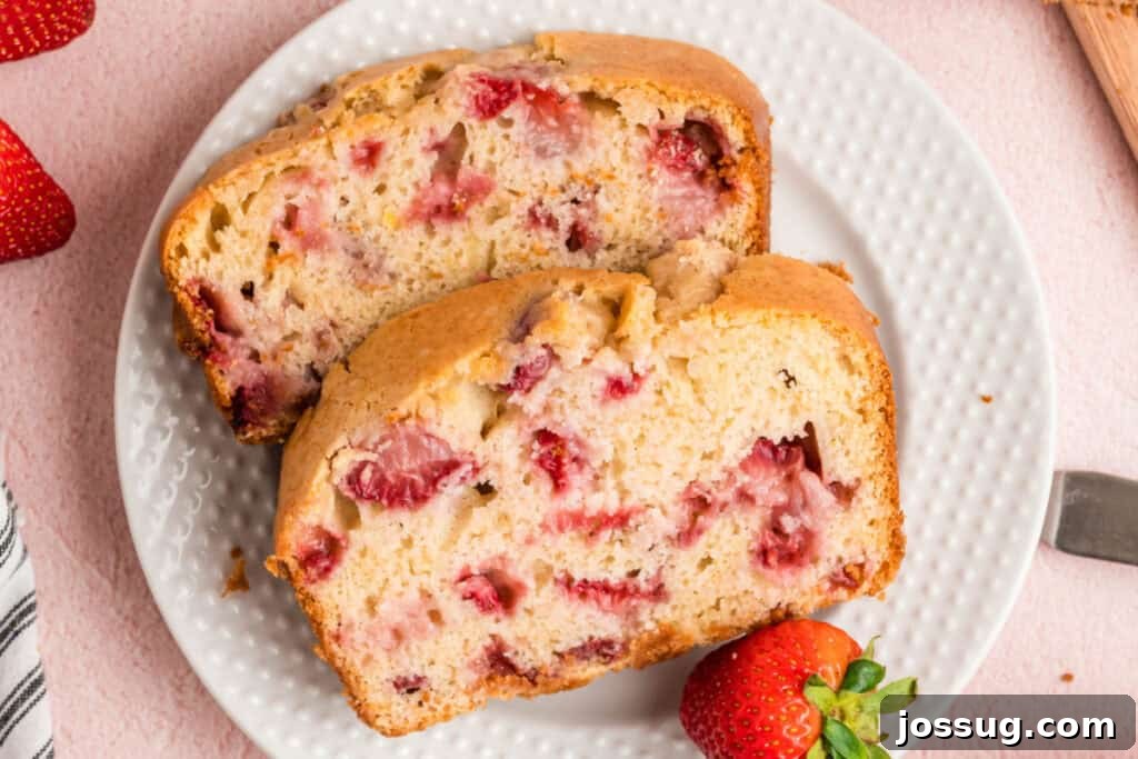 Sweet Strawberry Loaf 17 Two thick, inviting slices of strawberry bread presented on a pristine white plate, accompanied by a fresh, vibrant whole strawberry for garnish.