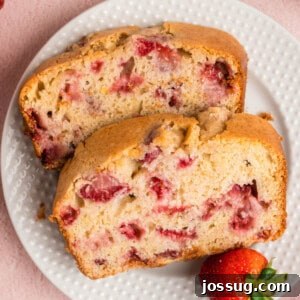 Closeup of two inviting slices of homemade strawberry bread on a white plate, showcasing the fluffy texture and juicy berry pieces.