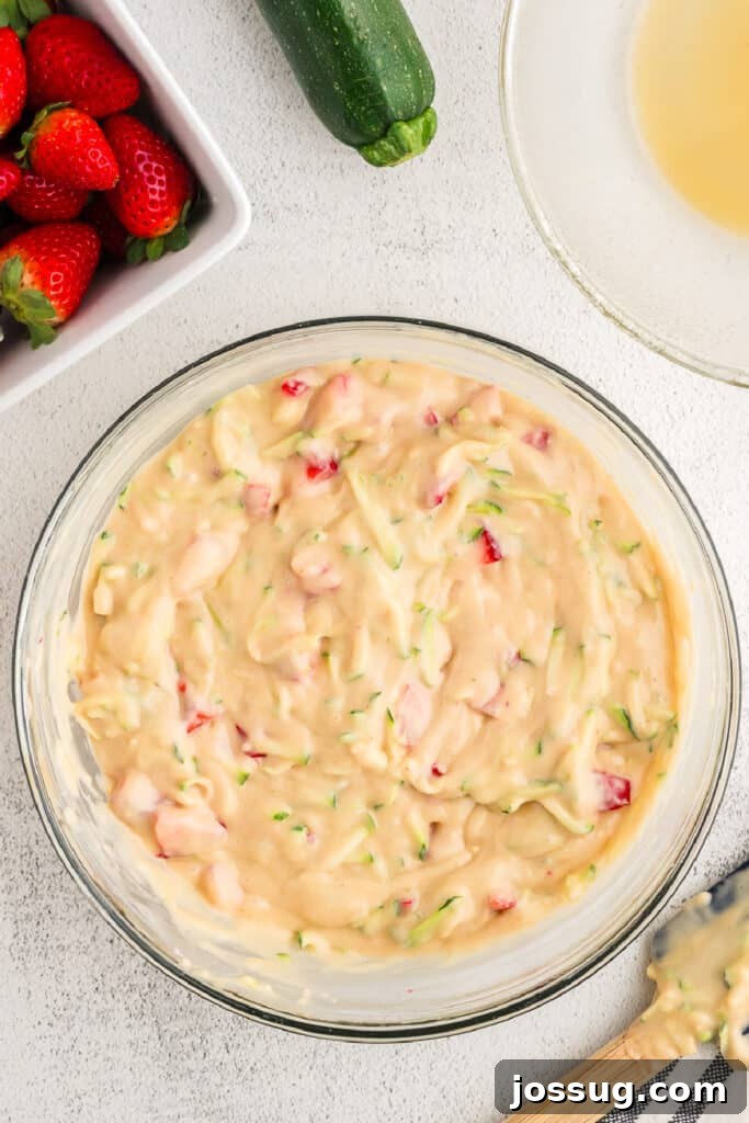 The strawberry zucchini bread batter is fully mixed with visible pieces of bright red strawberries and green zucchini evenly distributed throughout.