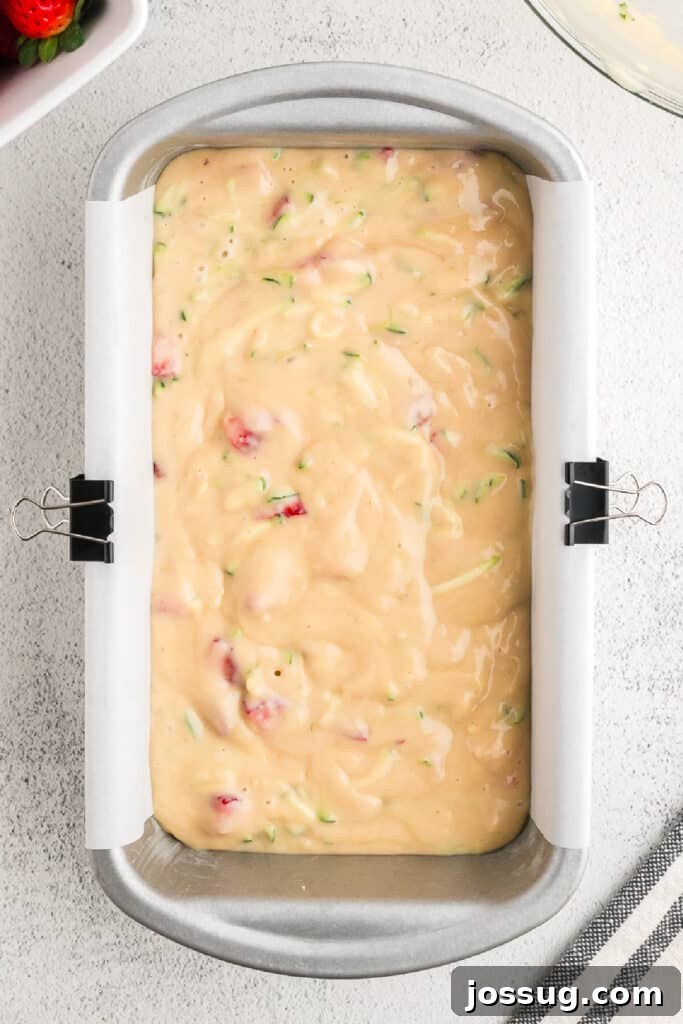 The unbaked strawberry zucchini bread batter is spread evenly into a parchment-lined loaf pan, ready for the oven to transform it.