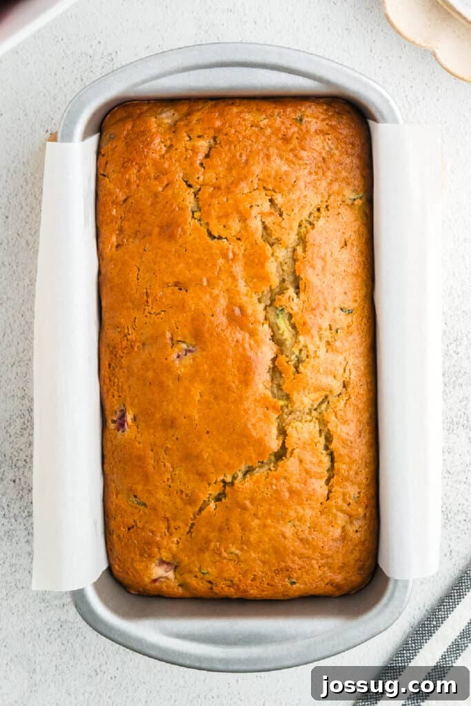 The golden-brown baked strawberry zucchini bread loaf, freshly out of the oven and still warm in its parchment-lined pan, looks perfectly cooked.